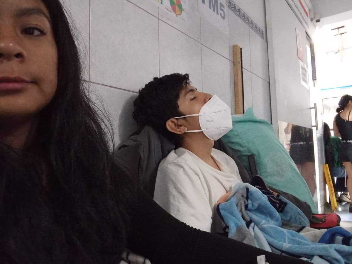 Joseph recostado con mascarilla en el pasadizo de emergencia junto a un familiar
