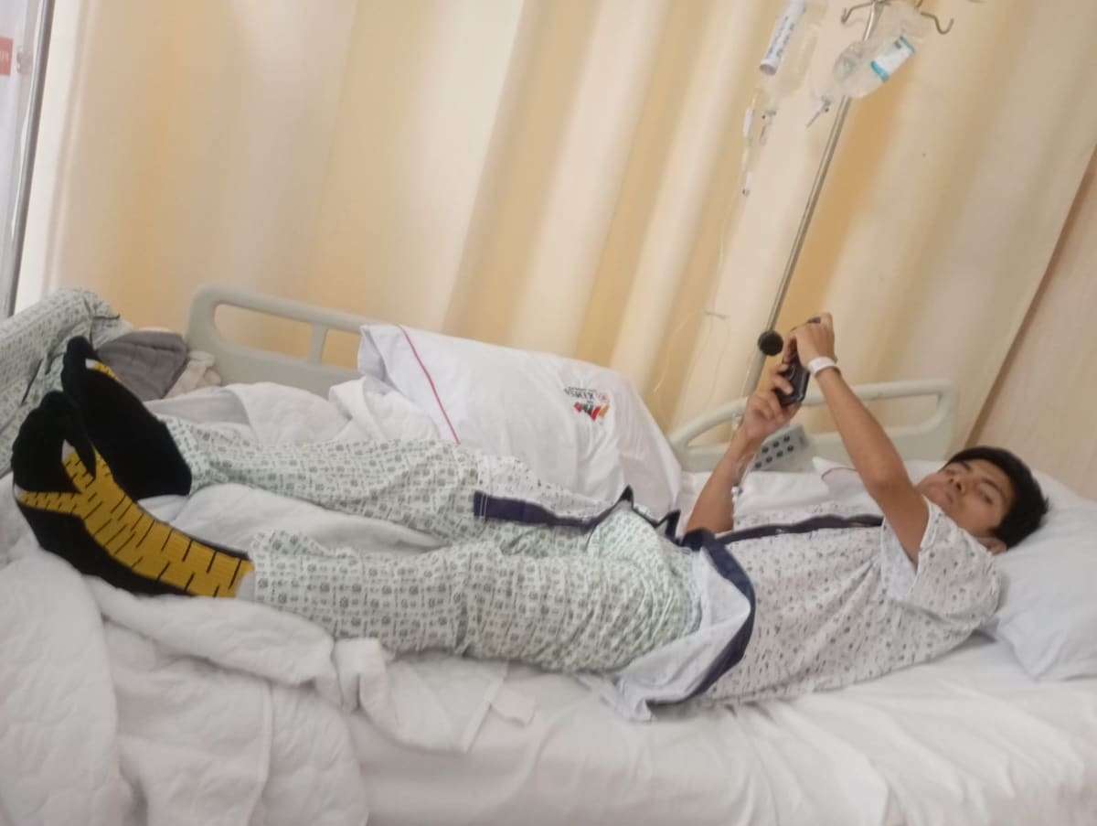 Joseph recostado en la cama de hospital con el celular en la mano