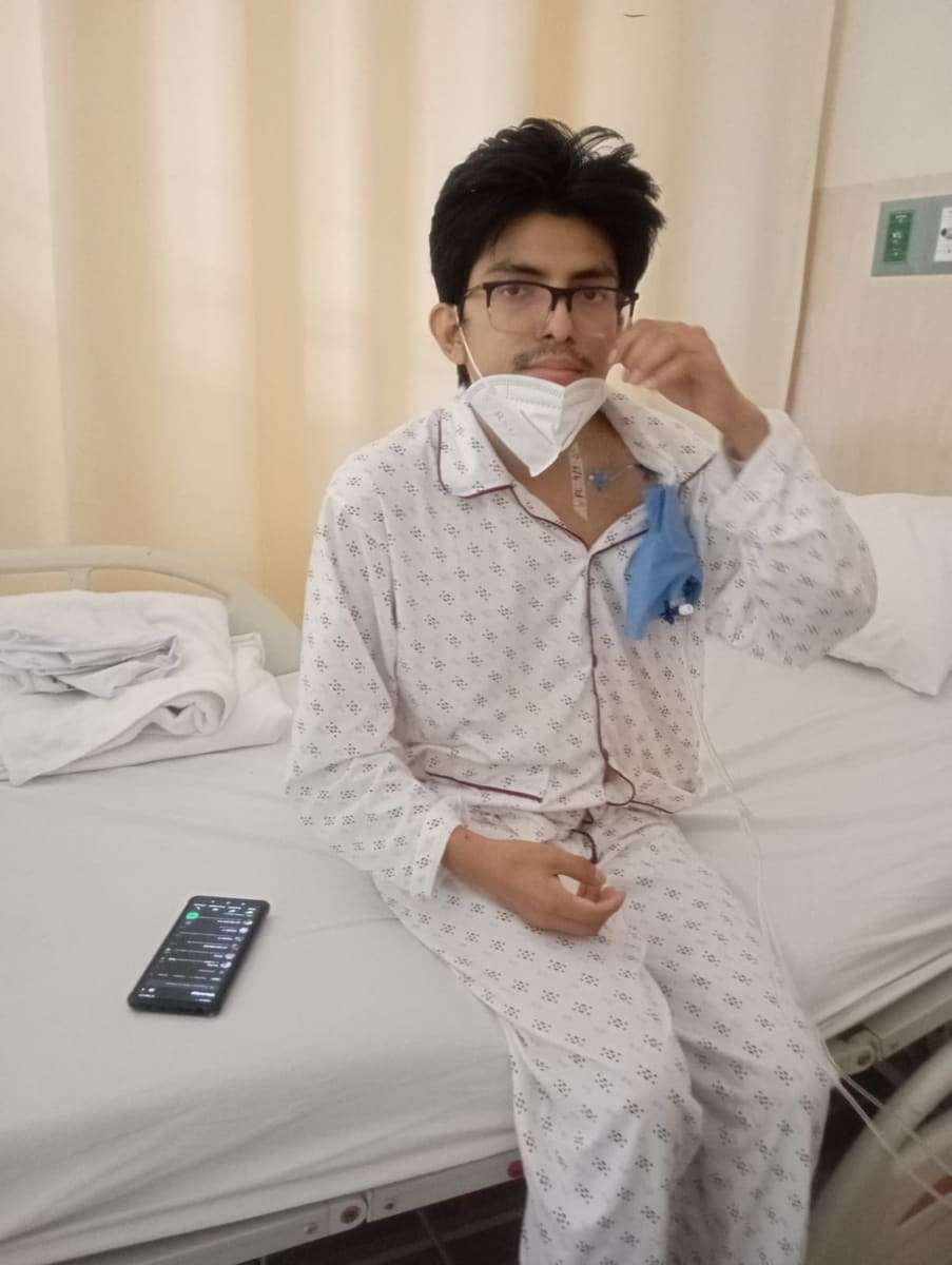 Joseph sentado en la cama bajándose la mascarilla y mirando a la cámara