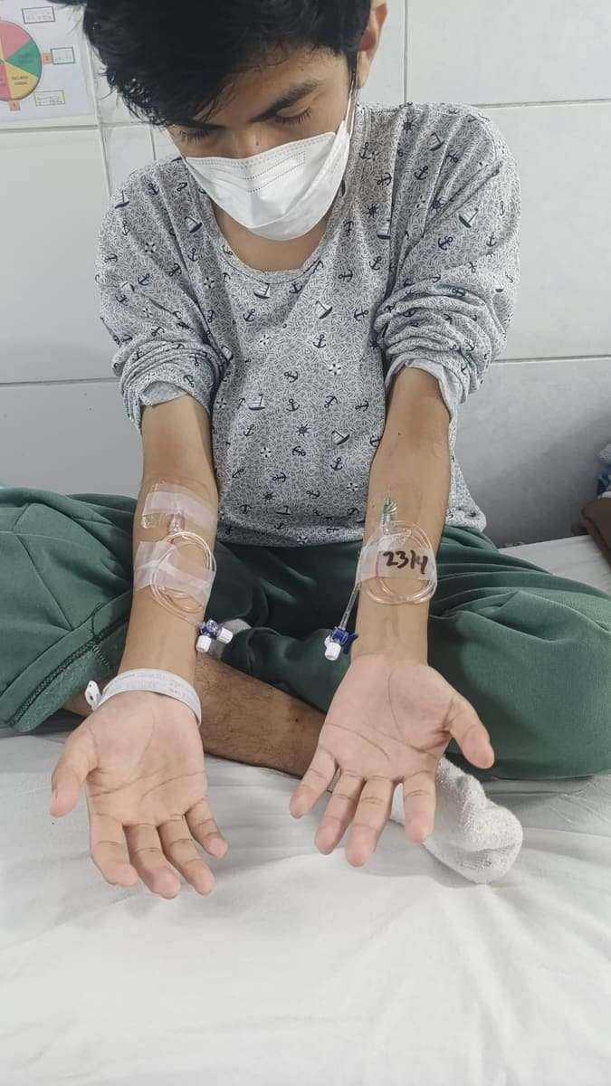 Joseph muestra sus dos brazos con vías y brazalete de hospital