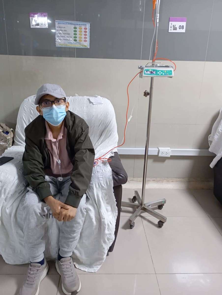 Joseph con gorra y mascarilla sentado junto al poste de suero en el hospital