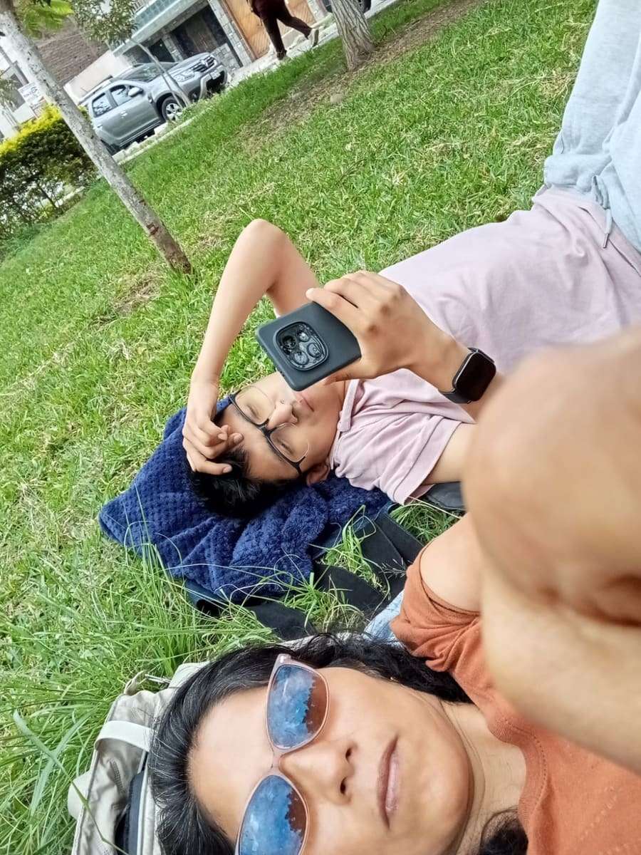 Joseph recostado en el césped con el celular, junto a su mamá
